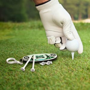 A golf tee set featuring white tees and a golf ball, with a logo on the holder. The hand is wearing a golf glove.