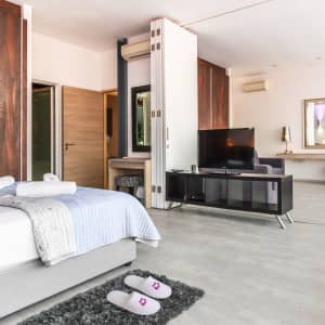 A pair of white hotel slippers placed on a grey rug in a modern hotel room with wooden furniture and a TV.