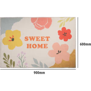 A floral plush mat in pastel colours featuring bright flowers and a central logo. Dimensions: 900mm x 600mm.