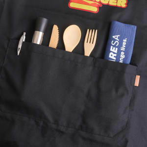 A black poly-cotton canvas apron with a pocket containing utensils and a towel, featuring a logo.