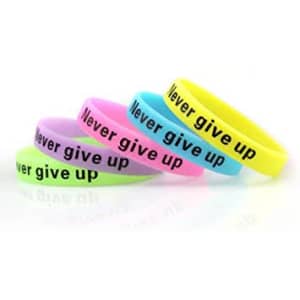 A collection of glow in the dark silicone wristbands in various colours with the phrase "Never give up" printed on them.