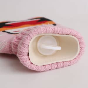 A pink hot water bottle with a knitted cover, featuring a cute design and a plastic opening at the top.