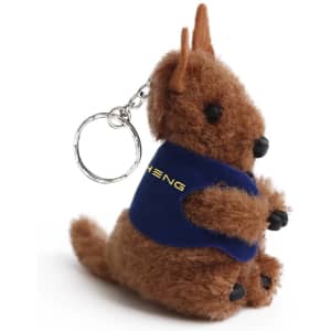A brown plush kangaroo toy with a keychain, featuring a blue vest and black accents, and a small branding logo.
