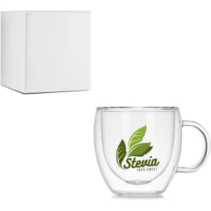 A clear glass double wall mug with a handle, accompanied by a plain white box. The mug features a green logo.