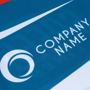 A close-up of a blue and white sports polo shirt featuring a logo. The material appears to be 100% polyester.