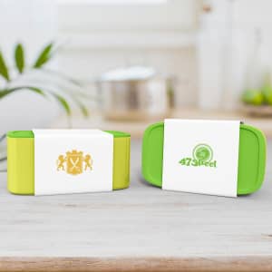 A green and yellow packaging sleeve surrounds two containers, featuring logos on the sides, set against a neutral background.