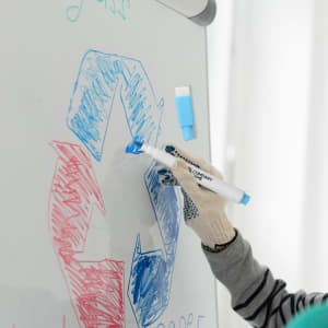 A blue magnetic whiteboard marker in use, with a gloved hand drawing on a whiteboard featuring colourful designs.
