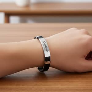 A black leather bracelet with a silver metal plate and a logo, resting on a wooden surface.