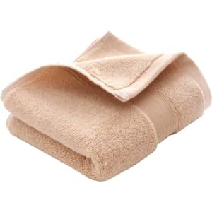 A folded beige cotton hand towel with a textured surface, featuring a logo on the side.