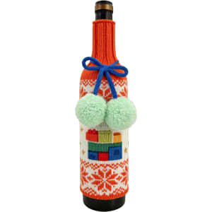 A drink bottle wrapped in a custom knitted sleeve featuring festive patterns, orange and white colours, and green pom-poms.