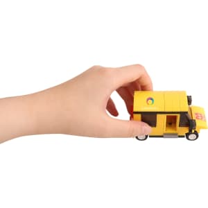 A hand holds a yellow toy delivery truck made of building blocks with a logo on the side.