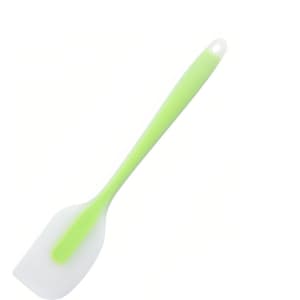 A silicone spatula with a white head and a green handle, featuring a hanging hole for easy storage.