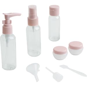 A set of clear toiletry bottles and jars with pink lids, including a pump, spray, and containers with a funnel and spatula.