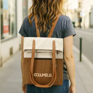A woman walks down the street carrying a convertible canvas backpack in cream and brown with shoulder straps.