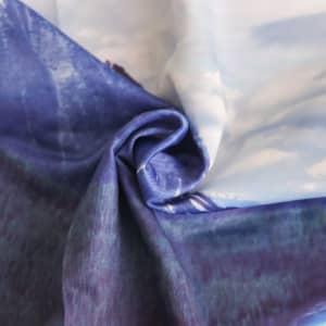 A close-up of a fabric featuring a blend of blue and purple tones, showcasing a silky texture and abstract design.
