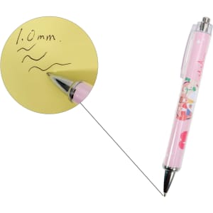 A pink ballpoint pen with a decorative design and silver tip, showcasing 1.0mm black ink writing on yellow paper.