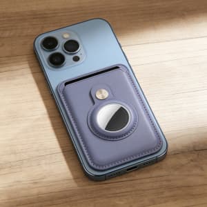 A lavender PU magnetic card and Airtag holder attached to a blue smartphone on a wooden surface.