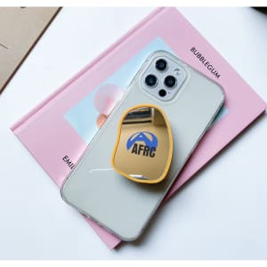 A yellow custom-shaped mirror phone pop holder on a clear phone case, resting on a pink book.