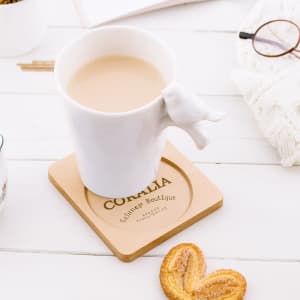 A wooden coaster with a square shape and circular center, featuring a light brown finish. It has a logo.
