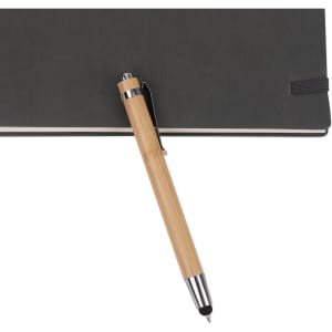 A bamboo pen with a stylus nib rests on a dark notebook, featuring a metal clip and shiny accents.