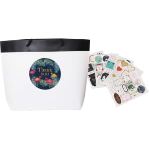 A small black and white boutique paper bag with a black rim and assorted decorative stickers beside it.