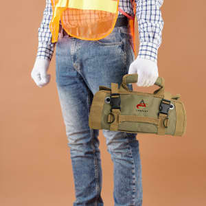 A khaki tool bag is held by a person wearing blue jeans and a safety vest, with gloves on.