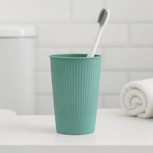 A teal wheat straw toothbrush cup with ridged texture, containing a white toothbrush, set on a bathroom counter.
