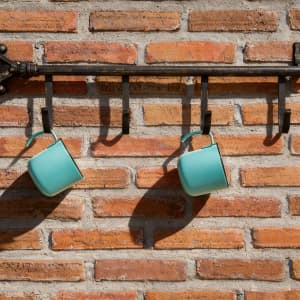 A drink bottle with an insulated design, featuring a light turquoise colour and a hanging loop, displayed on a brick wall.