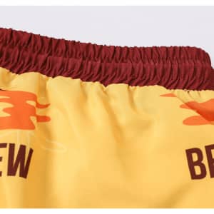 Men's polyester board shorts in yellow with maroon elastic waistband, featuring a logo and colourful graphics.