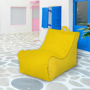 A yellow outdoor chair sits on a stone-paved surface near blue and pink doors, featuring a simple logo.