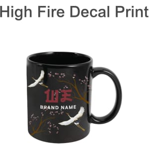 A black mug featuring a decorative design with cranes and floral elements. It has a brand logo.