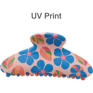 A floral hair clip featuring a pink background with blue flowers and colourful leaves, designed with UV print.