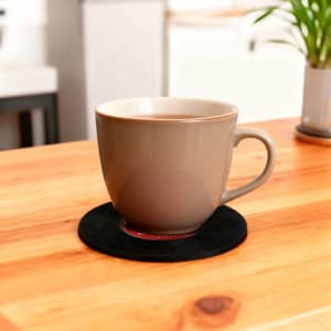 A drink bottle rests on a black custom record coaster on a wooden table, with a plant in the background.