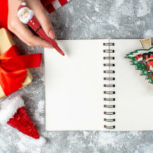 A red pen featuring a Santa stress reliever, surrounded by gifts, a blank notebook, and festive decorations.