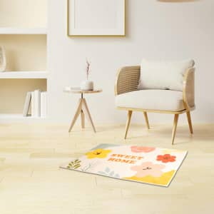 A plush logo mat featuring colourful floral designs, placed on a wooden floor next to a minimalist chair and table.