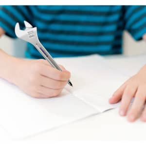 A spanner-shaped ballpoint pen in silver, being held by a person writing on a sheet of paper.