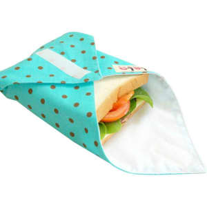 A reusable food wrap in aqua with white polka dots, partially covering a sandwich with lettuce and tomato.