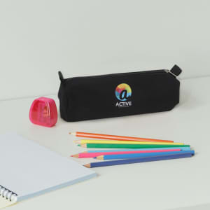 A black canvas pencil case with a logo, surrounded by coloured pencils and a pink sharpener on a desk.