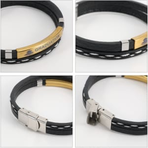 A black leather bracelet featuring a gold bar with branding. The design includes white stitching and a metallic clasp.