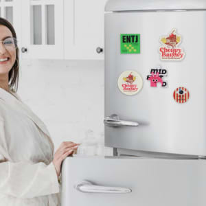 A fridge covered with colourful acrylic magnets depicting various designs, alongside a person interacting with the fridge.