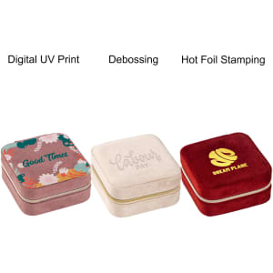 Three square velvet jewellery organisers in pink, cream, and red with decorative designs and a logo on each.