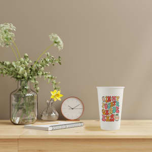Custom disposable single wall paper cup featuring a colourful design, set on a wooden surface with a clock and plants.