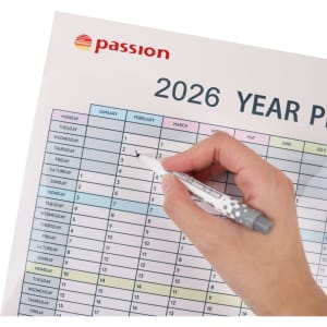 A hand holding a grey pen marks a date on a colourful 2026 year planner with a logo in the corner.