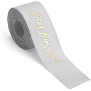 A roll of grey cotton ribbon featuring a gold hot stamped design. Includes a logo on the side.