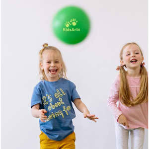 A green inflatable PVC ball mid-air, with two children smiling and playing in the background. One child wears a blue shirt, and the other wears a pink top.