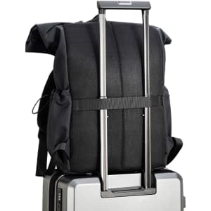 A black polyurethane roll top backpack resting on a suitcase with an extended handle, showcasing its design and features.