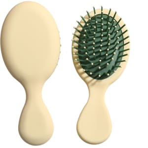 A mini paddle brush with a cream handle and green bristle base, featuring a logo on the handle.