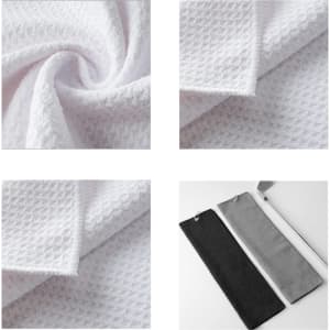 A waffle-textured golf towel in white, folded and displayed with a black and grey towel alongside. Features a branding logo.