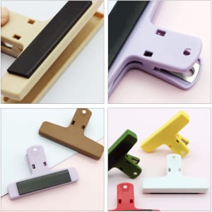 Plastic magnetic clips in various colours: beige, purple, brown, green, yellow, and white. Includes a logo on the clips.