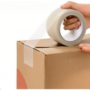 A hand holds a roll of transparent BOPP packaging tape while applying it to a cardboard box.